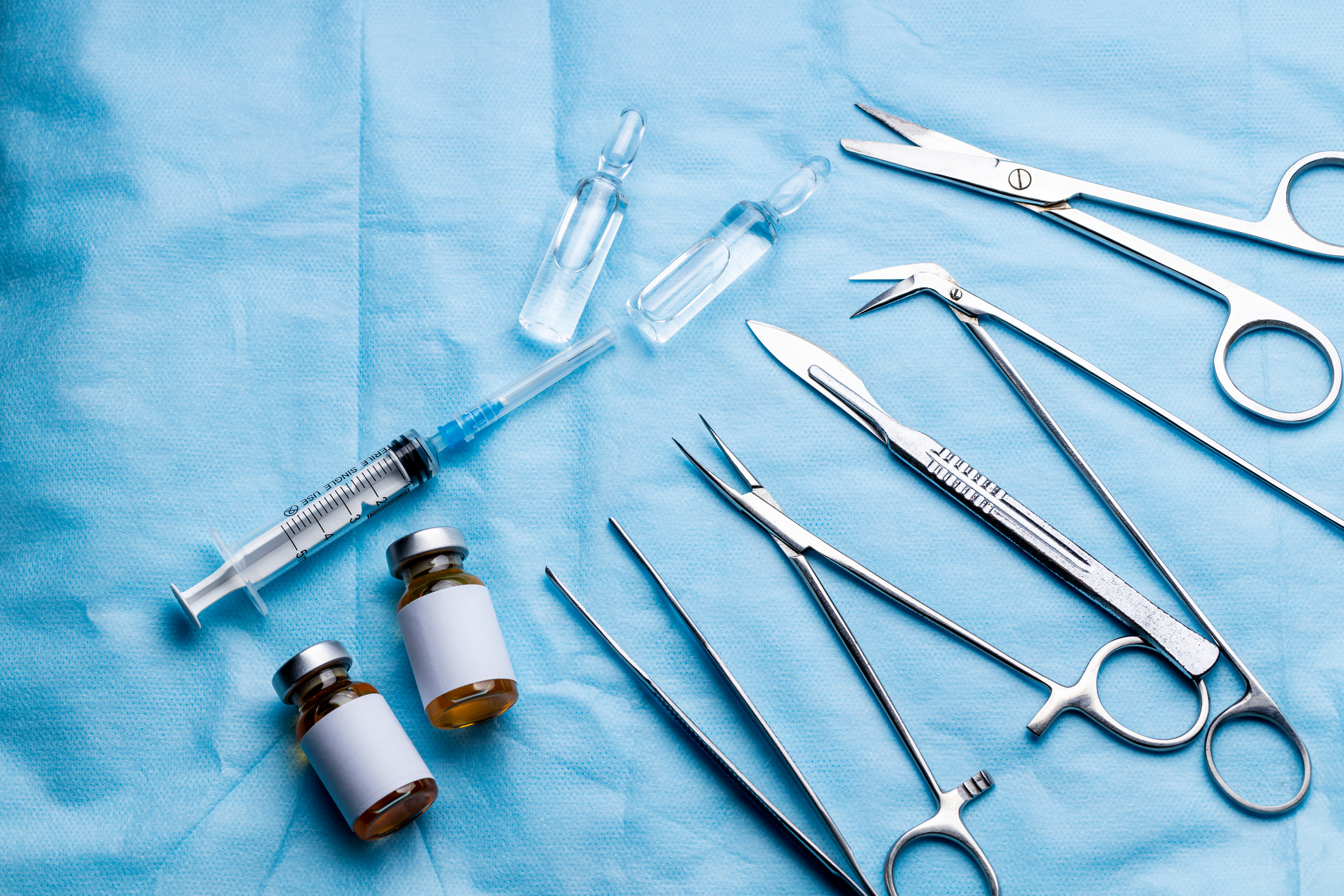 stack of surgical equipment at surgery desk. medical tools such scissors, scalpel, forceps, tweezers over blue background. surgery concept